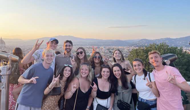 A group of students pose in front of a view Florence, Italy at sunset.