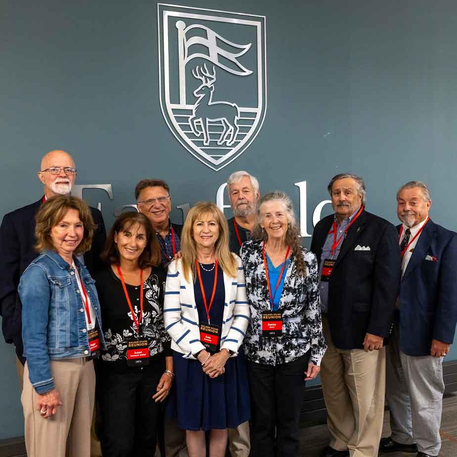 A large group posed in front of the Fairfield University shield in the Dogwood Room.