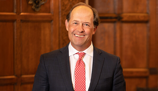 Photo of President Mark R. Nemec, PhD standing in front of a dark wooden background.