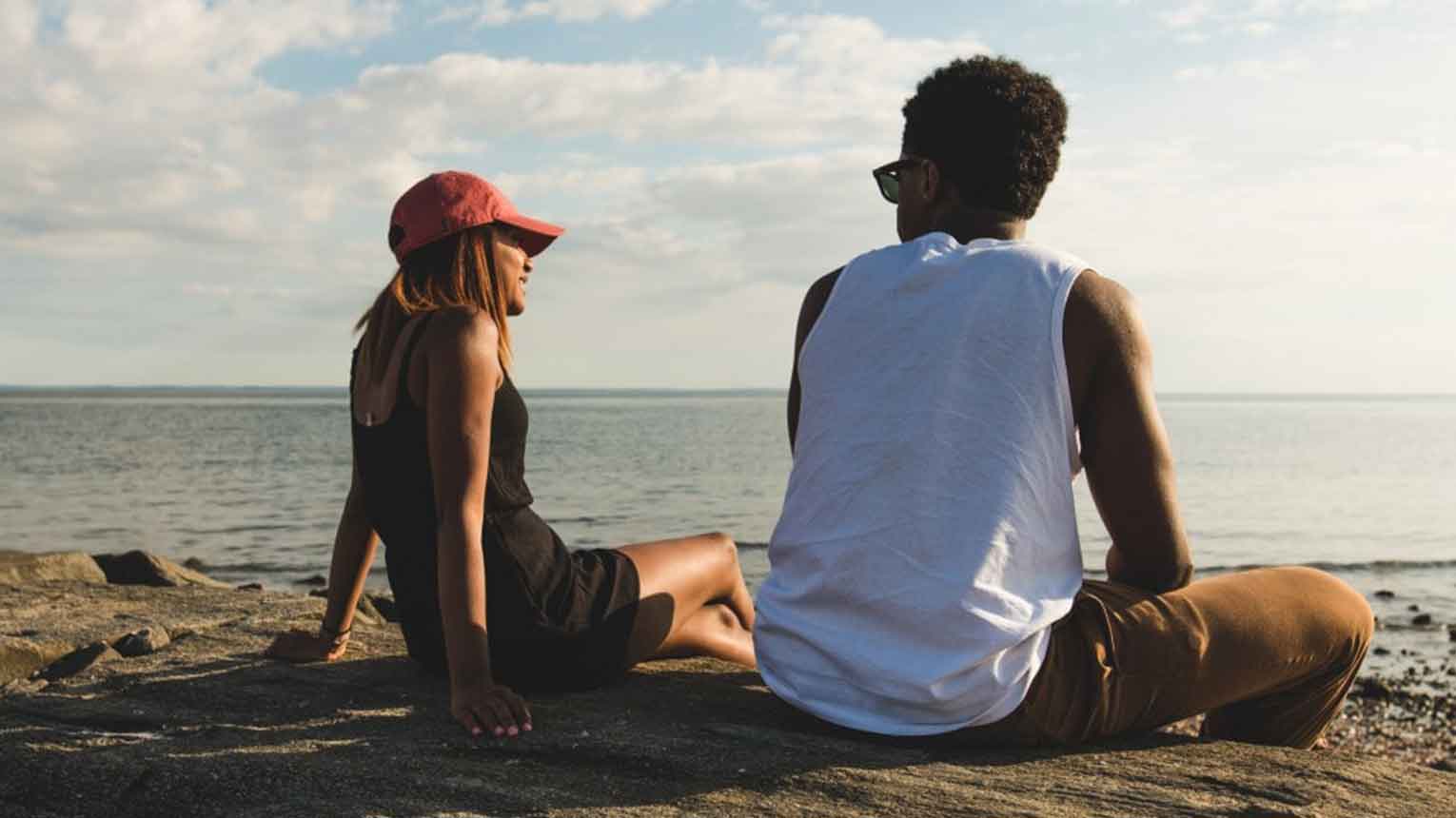 Two students sitting side by side talking at the beach.