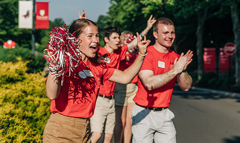 A lively group of people wearing red shirts, holding pom poms, cheering enthusiastically together.