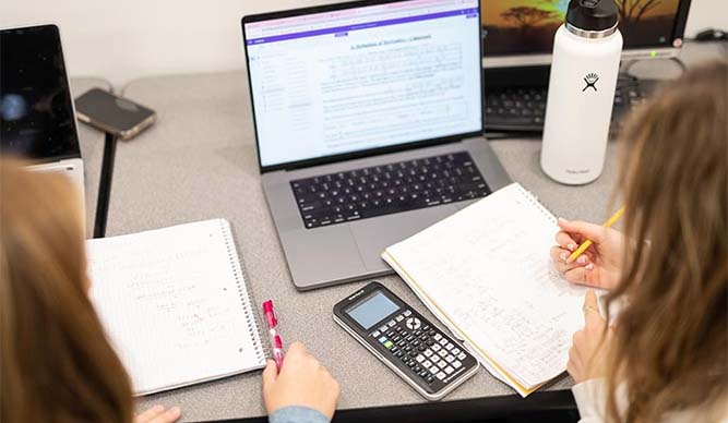 Students working together and doing calculations with notebooks and a calculator.