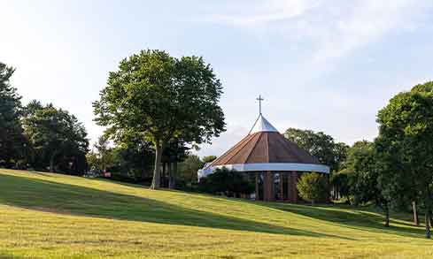 A building with a cross on top in the distance surrounded by trees and hills. 
