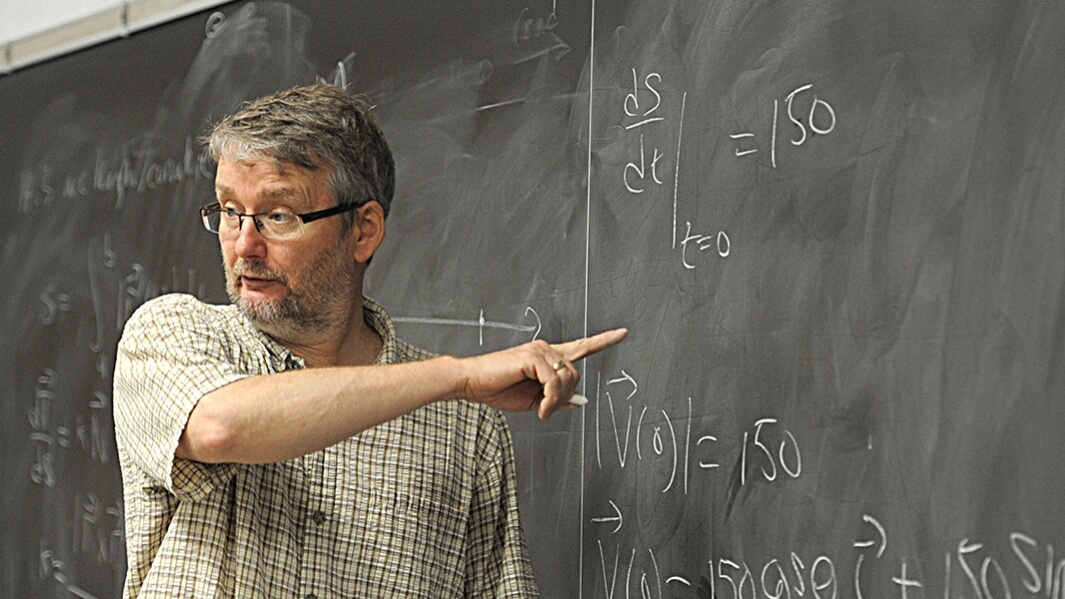 Professor of Applied Statistics teaching and pointing at black board. 