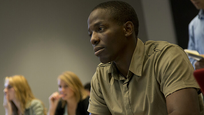 A black studies student sitting in a lecture class looking focused.