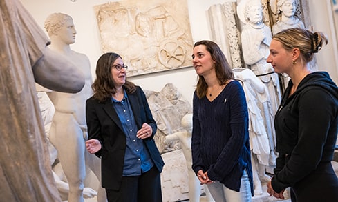 Professor showcasing a stone statue in an exhibition to two interested students.