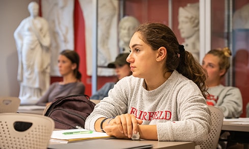 Students listening to a lecture in a history class with stone statue replicas behind them.