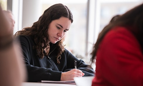 Student taking diligent, handwritten notes while in class.