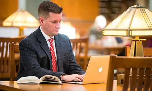 A man sitting at a table, focused on a laptop in a well-lit room. 