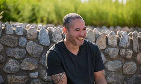 A man sitting on a bench, smiling warmly at the camera, enjoying a sunny day on campus. 