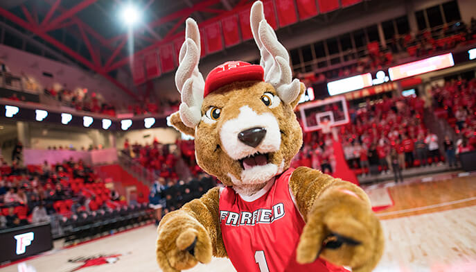 Lucas the Stag mascot, clad in a red jersey, poses on the basketball court, embodying team spirit and enthusiasm.