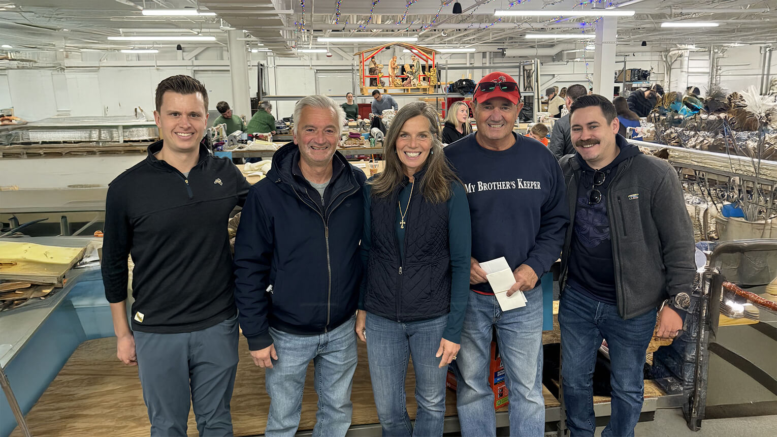 Five individuals, including a man and a woman, stand together in a factory setting, showcasing teamwork and collaboration.