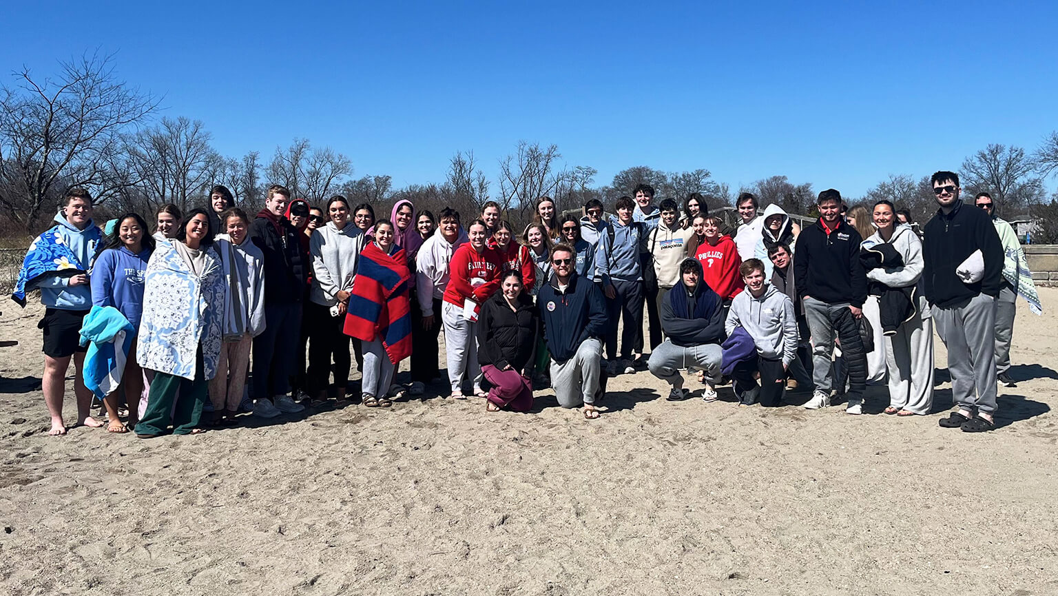 Several individuals gathered on the beach, with a vibrant blue sky overhead, creating a cheerful atmosphere.