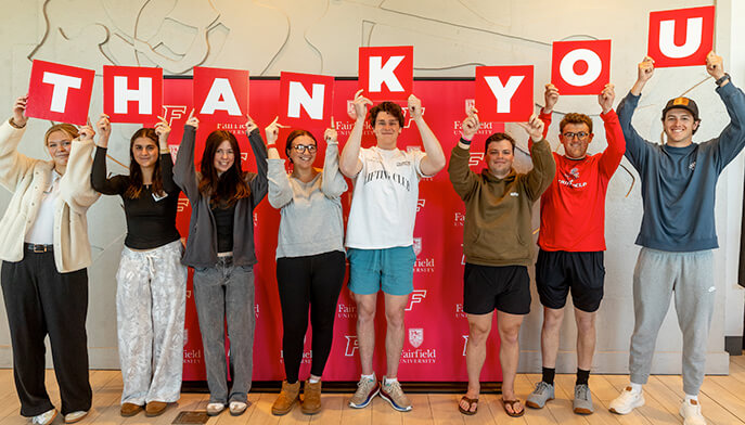 A diverse group of people smiling and holding up colorful signs that spell out "Thank You". 