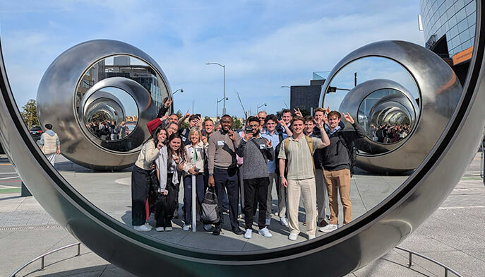 People standing together, smiling in front of a large sculpture with joyful expressions. 