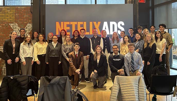 Big group of students stand and kneel in front of digital Netflix sign.