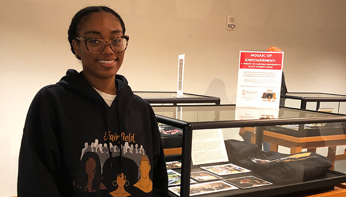 A female student wearing a black sweatshirt stands in front of a display case, observing the items inside. 