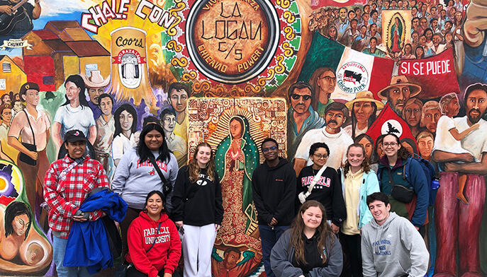 A diverse group of students poses together in front of a colorful mural, showcasing vibrant artwork and community spirit. 