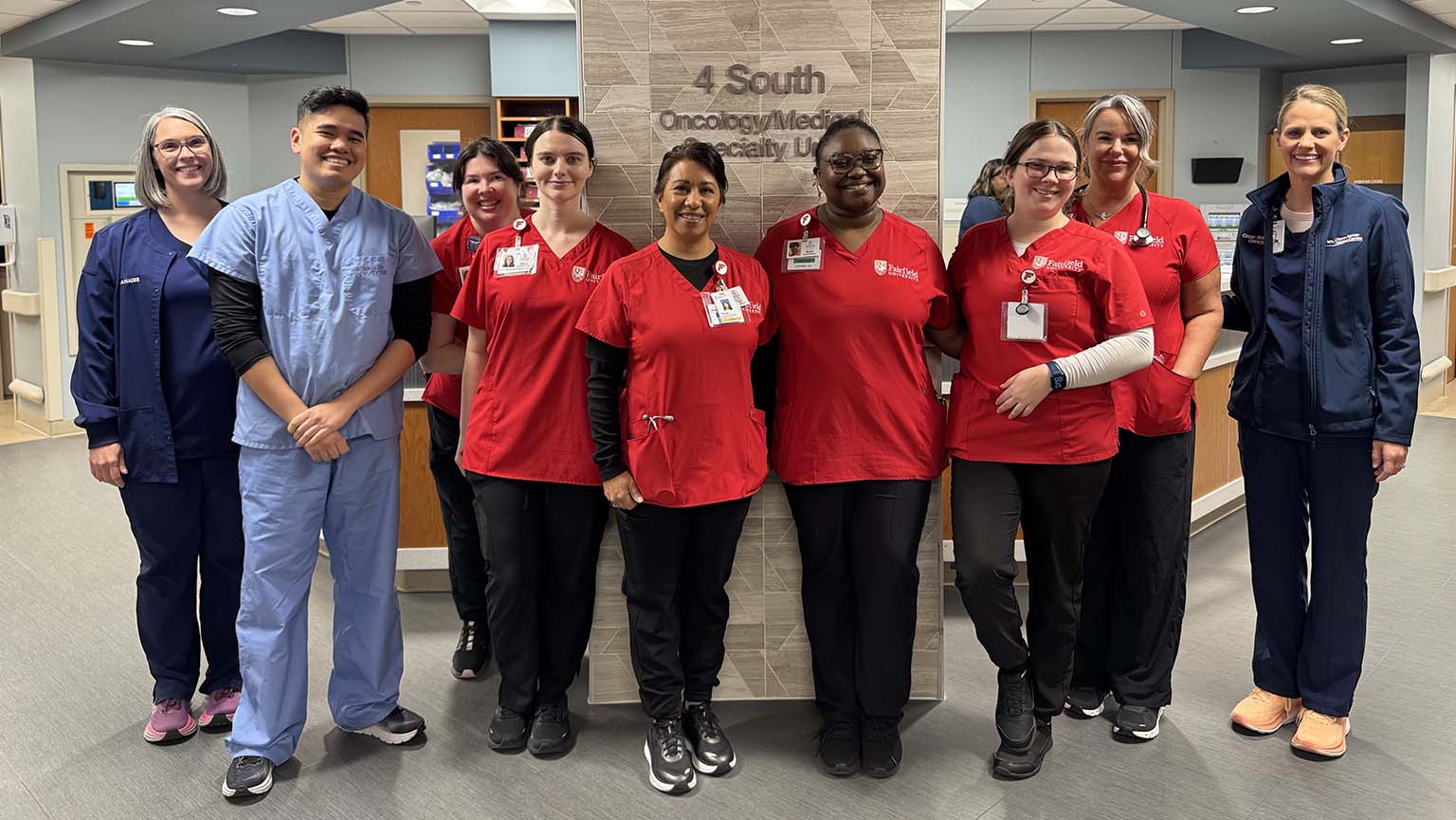 Image of a group of nurses smiles together in front of a hospital sign.