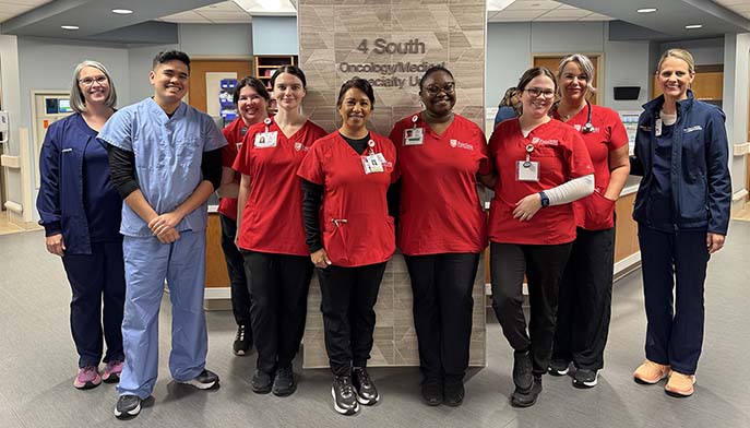 Image of a group of nurses smiles together in front of a hospital sign.