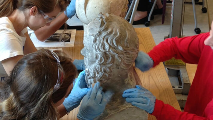Art History & Visual Culture students molding the head of man with a long beard.