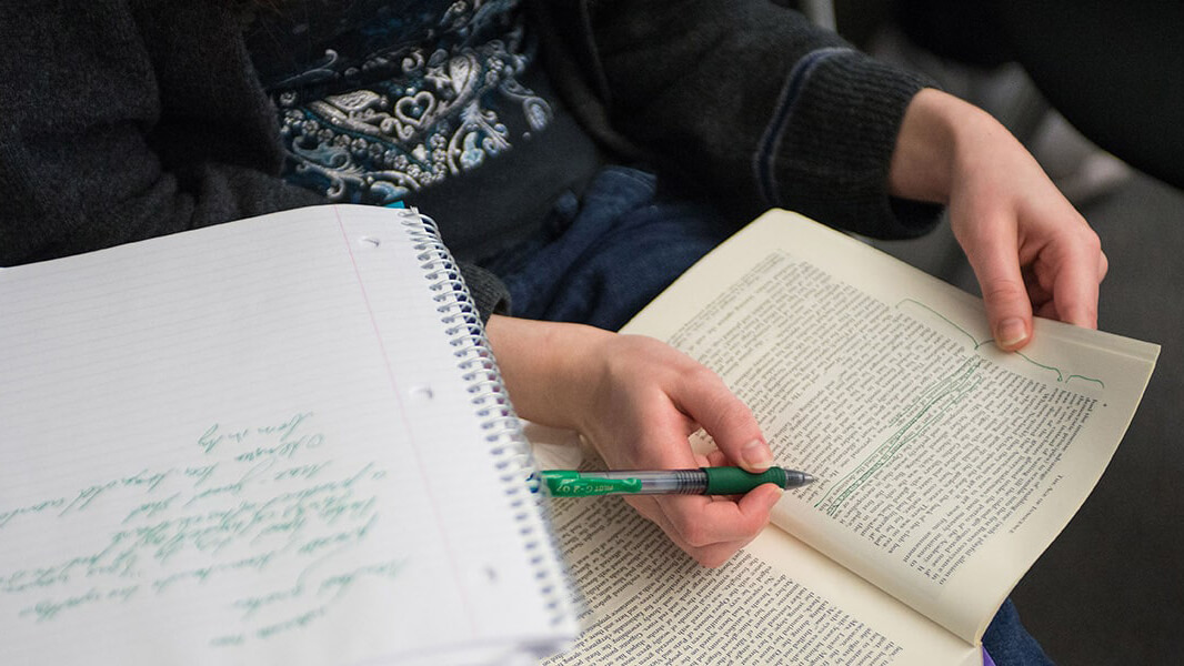 Closeup of a student's notebooks with them highlighting a text in green.