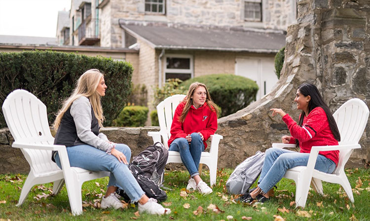 Students sitting around in adirondack chairs talking outside. 