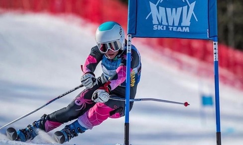 A person on skis, leaning slightly forward coming down slope. 