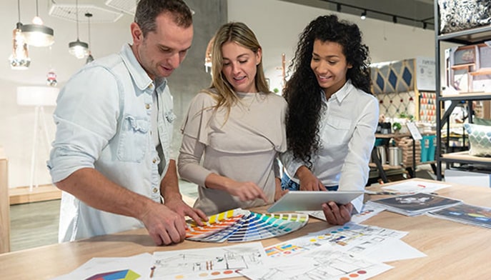 A group of three interior designers working together at a studio, looking a color swatches and plans with a tablet.