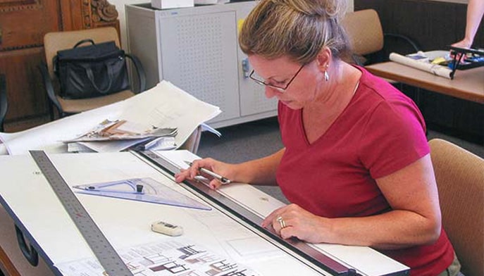 Interior designer sketching a design plan, using a ruler at her desk.