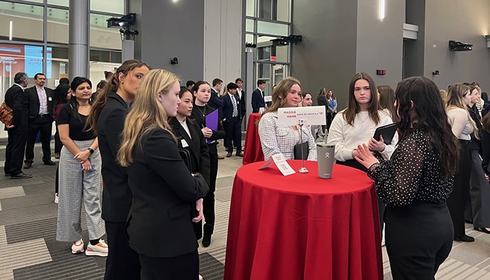 Female business students chatting with and learning from a Bank of America employee at a campus event.